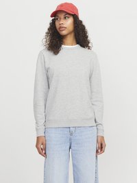 Szara bluza z miękkiego materiału z okrągłym dekoltem. Połączona z jasnoniebieskimi spodniami typu wide-leg i czerwoną czapką z logo.