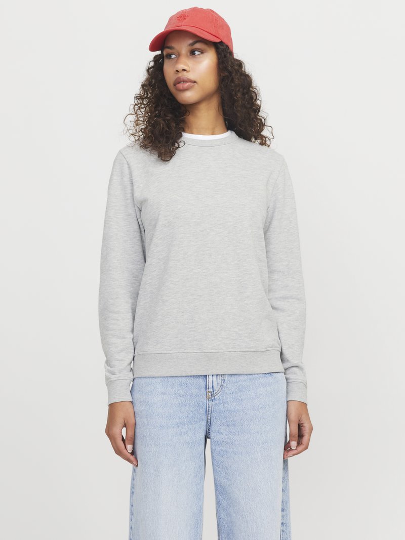 Szara bluza z miękkiego materiału z okrągłym dekoltem. Połączona z jasnoniebieskimi spodniami typu wide-leg i czerwoną czapką z logo.