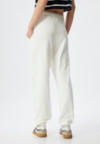 Cremefarvede sweatpants med en afslappet pasform, elastisk talje, sidelommer og ribbede manchetter, parret med afslappede sneakers.