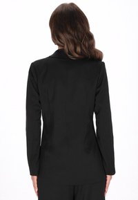 Zwarte op maat gemaakte blazer met een notch lapel, lange mouwen en een getailleerde silhouet. De gladde textuur en strakke lijnen versterken de professionele uitstraling.