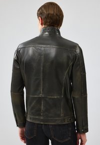 Veste en cuir noir au fini lisse, dotée d'un col montant, de coutures décoratives et d'une coupe ajustée. Accentuée par des pressions.