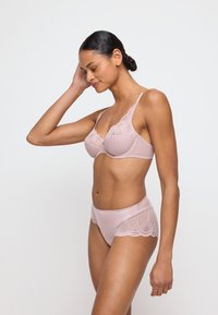 Jasnoróżowy zestaw bielizny składający się z koronkowego biustonosza o geometrycznym wzorze oraz dopasowanych majtek z wysokim stanem ozdobionych koronką. Gładka tekstura.