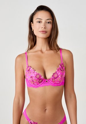Lacy pink bra featuring floral embroidery, adjustable straps, and a plunging neckline. Designed with a small central keyhole detail.