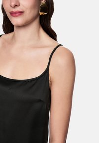 Black satin camisole with thin straps, featuring a smooth texture and slight sheen. Gold oversized earrings add contrast.