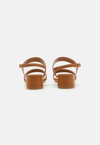 Sandalias de cuero marrón con tacón cuadrado y múltiples correas entrelazadas, que presentan un detalle de hebilla dorada en la correa del tobillo.