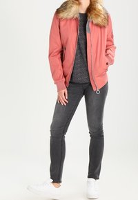 Světle růžová bomber bunda s umělou kožešinou na límci, zapínací kapsy, v kombinaci se tmavě šedými džínami a bílými teniskami. Hladká látka, volný střih.