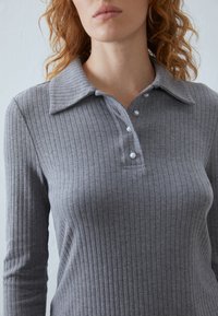 Grijze geribbelde langemouwen polo met een gekraagde hals, voorzien van drie parelachtige knopen langs de sluiting. Zachte stoftextuur.