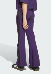 Purple flared pants made from soft fabric. Features black side stripes and a comfortable fit, paired with black and white shoes.