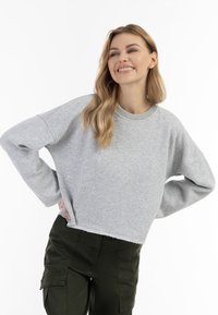 Šedá zkrácená mikina s kulatým výstřihem a spadlými rameny, vyrobená z měkké látky. V kombinaci s olivovými cargo kalhotami.