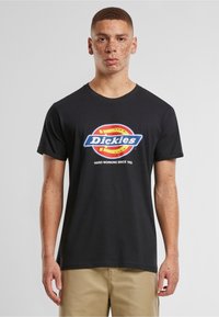Juodas medvilnės marškinėliai su apvaliu kaklu ir trumpomis rankovėmis, su margu "Dickies" logotipu ir tekstu "DIRBANTYS SUNKIAI NUO 1922".