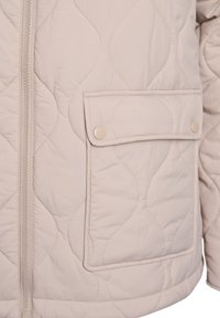Lysebeige quiltet jakke med lynlås foran, sidelomme med trykknap og en glat tekstur med bølgemønster.