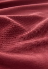 Tissu texturé d'un rouge profond, présentant un motif tissé subtil avec de légers plis, mettant en valeur sa nature légère et souple.