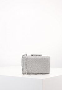 Lille rektangulær sølvfarvet clutch med tekstureret metaloverflade og tynd kædestrop, placeret på en hvid sokkel mod en ensfarvet baggrund.