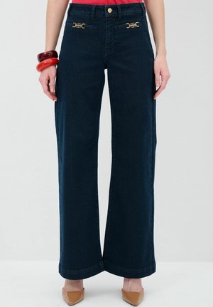 Hoch taillierte, weit geschnittene, dunkelblaue Jeanshose mit goldenen Hardware-Akzenten und einem enganliegenden Taillenbund, kombiniert mit einem schlichten Oberteil.