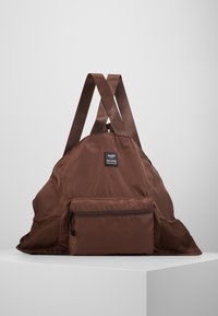 Brun nylonryggsäck med meshnätfickor på sida, justerbara platta axelremmar och en framficka med zip. Har ett tygmärke upptill.