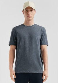 T-shirt gris à manches courtes en tissu doux, avec un col rond et une coupe décontractée, porté avec une casquette de couleur claire.
