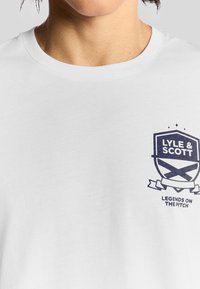 Hvid bomulds T-shirt med et grafisk logo i marineblå farve, der har teksten "LYLE & SCOTT" samt "LEGENDS ON THE PITCH" i et skjold-design.