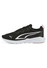 Zapatilla deportiva negra con upper de malla texturizada, suela blanca y logotipo y acentos blancos en contraste. Presenta cordones y una lengüeta trasera.