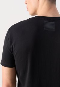 Black cotton t-shirt with short sleeves, featuring a subtle horizontal stripe detail on the upper back. Soft texture, casual fit.