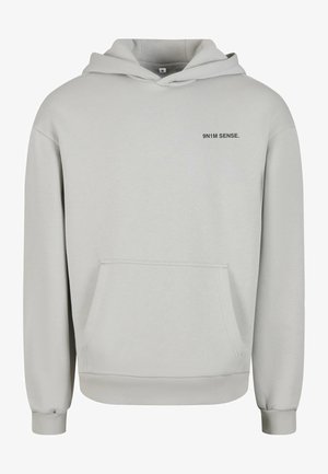 Gaiši pelēks kapuci, kas izgatavots no mīksta auduma, ar priekšējo kabatu, kapuci ar auklu un nelielu melnu tekstu "9N1M SENSE." uz krūšu.
