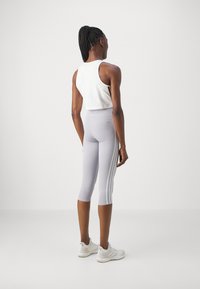 Fehér, rövidített sporting viselt szürke háromnegyedes leggings-szel, amelyeken fehér csíkok futnak az oldalakon, mindezt fehér edzőcipőkkel egészítjük ki.