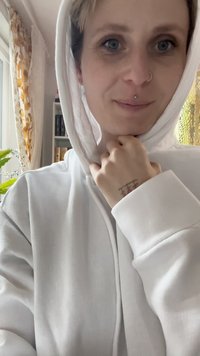 Igračka pamučna dukserica bijele boje s kapuljačom na vezanje, vidljivim detaljima šivanja i tetovažom na zapešću. Unutrašnji prostor s mekim osvjetljenjem.