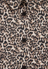 Audinio su leopardo raštu, juodais mygtukais ir matomomis siūlėmis mygtukais uždarytame drabužyje.