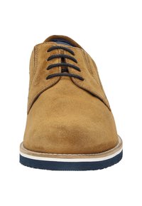 Chaussure en daim marron avec un bout arrondi, des lacets noirs et une semelle intermédiaire blanche contrastante avec une semelle extérieure en caoutchouc bleu foncé.