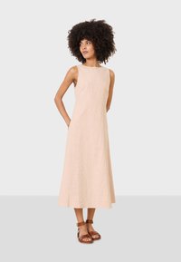 Vestido de lino color beige claro con un diseño sin mangas y una larga falda fluida. Combinado con sandalias de cuero marrón con correas en el tobillo.