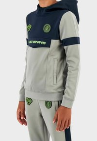 Grijs en marineblauw tweedelig trainingspak met capuchon, voorzien van neon groene logo's en accenten. Soepele stof met zijzakken en aangesloten manchetten.