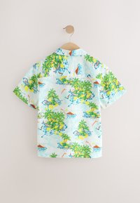 Chemise à manches courtes en tissu bleu clair avec un motif de paysage tropical comprenant des palmiers, de l'eau et des bateaux. Texture lisse et coupe décontractée.