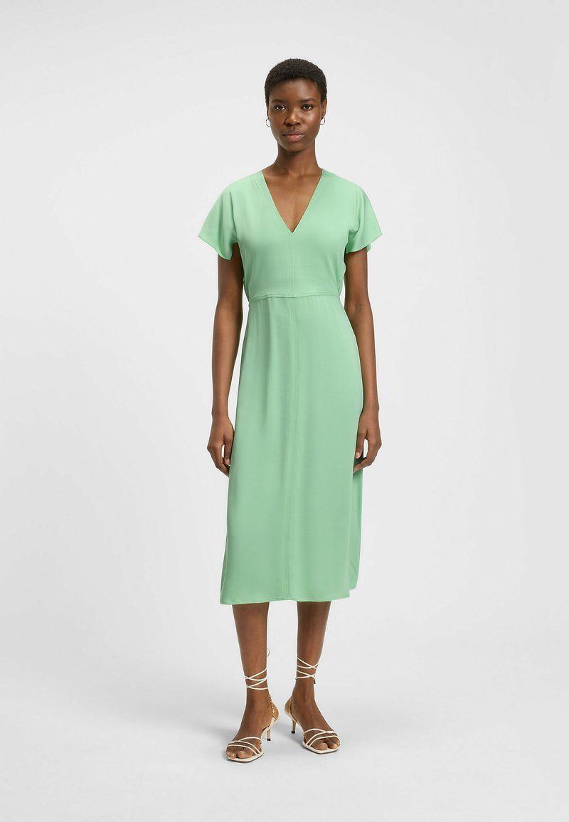 Mint green midi-mekko, jossa on lyhyet leijuvat hihat, syvä V-pääntie ja tiukka vyötärö. Sujuva kangas, jossa on kevyt kiilto.