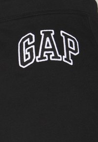 Tessuto nero con logo "GAP" ricamato in bianco. Texture liscia, stile casual, con scollatura arrotondata e una vestibilità classica.