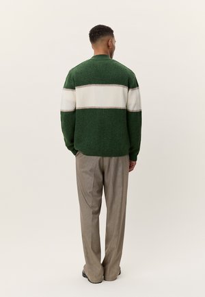 Pruhovaný svetr v zelené a krémové barvě s žebrovanou texturou, nošený s béžovými kostkovanými kalhotami. Na zádech jednoduchý, ležérní design.