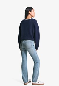 Marineblauwe trui met een relaxte pasvorm en geribde halslijn, gecombineerd met lichtgewassen rechte jeans en witte sneakers met bruine accenten.