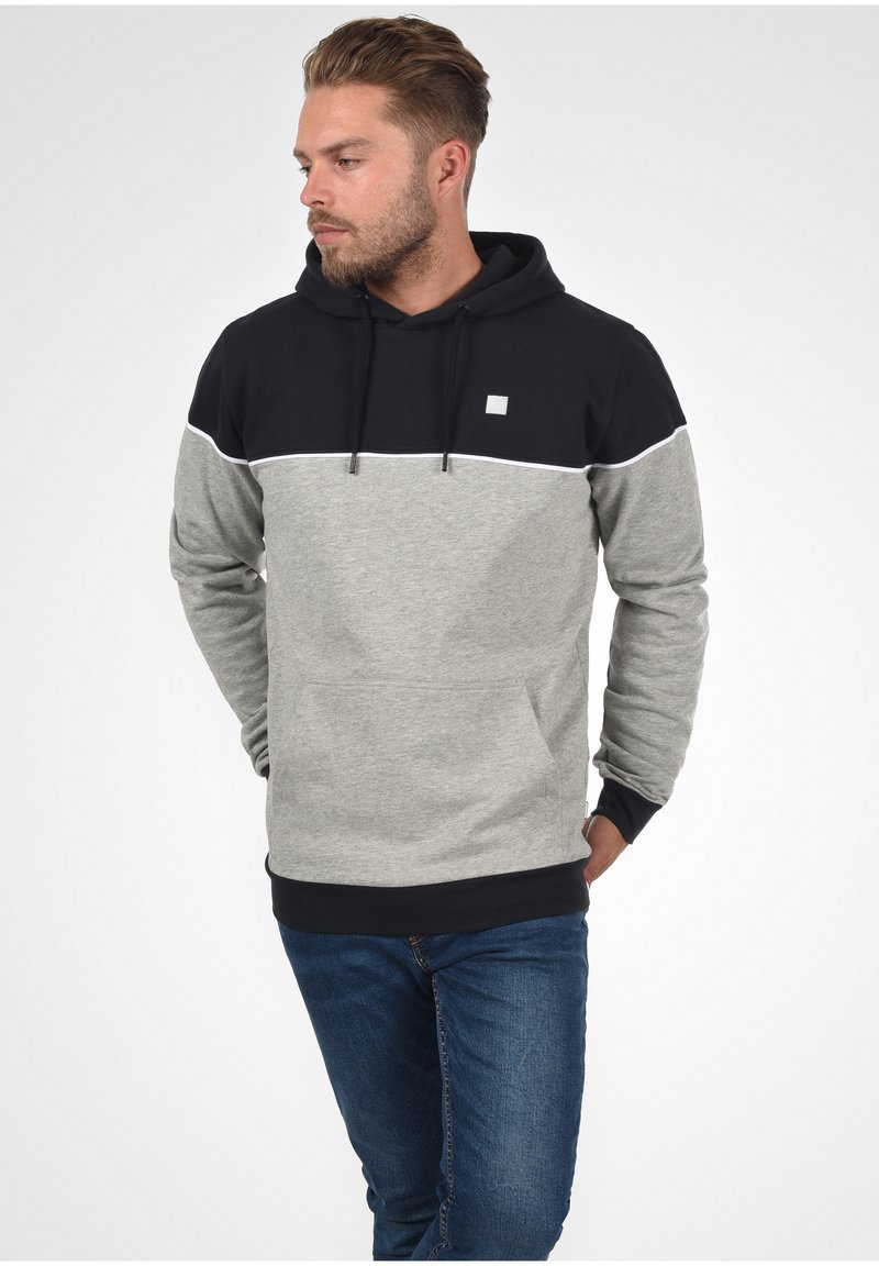 Hoodie met een zwart bovenste gedeelte en een grijs ondergedeelte, voorzien van een voorzak, een witte accentlijn en een klein logo op de borst.