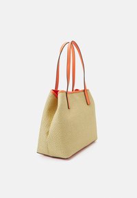 Żółta pleciona torba na ramię z pomarańczowymi skórzanymi uchwytami, zaokrąglonymi rogami i kontrastującym czerwonym dnem. Teksturowany materiał z widocznym wzorem plecionki.