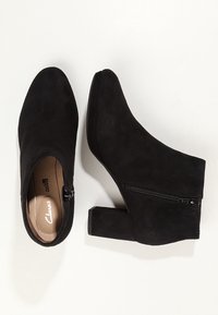 Botines negros de ante con puntera redonda, cremallera lateral y tacón grueso, que cuentan con una textura suave y un diseño minimalista.