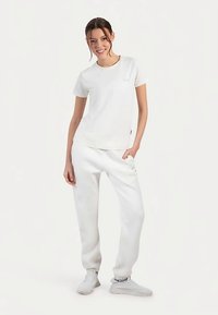 Weißes Baumwoll-T-Shirt mit kurzen Ärmeln und einer kleinen Taschenapplikation, kombiniert mit passenden weißen Jogginghosen und weißen Turnschuhen.