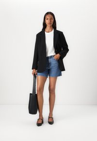 Svart oversized blazer, hvit t-skjorte, denimshorts, svarte leiligheter, og en svart totebag. Enkelt design med en avslappet passform. Glatte teksturer.