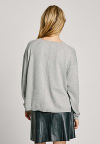 Pull gris surdimensionné avec manches raglan et poignets côtelés, associé à une jupe en cuir vert foncé avec des coutures verticales.