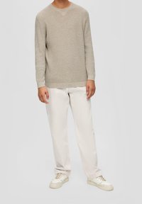 Maglione beige a trama con maniche lunghe e scollatura a girocollo, abbinato a pantaloni chiari e sneakers crema.