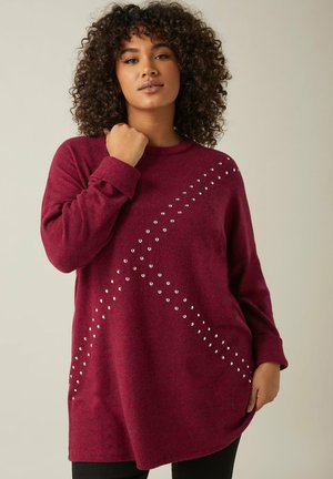Burgunderfarbener oversized Pullover mit weicher Textur, der silberne Nieten zeigt, die in einem diagonalen Muster entlang einer Seite angeordnet sind, sowie gerippte Bündchen.