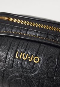 Schwarze, strukturierte Lederhandtasche mit goldenem Reißverschluss und eingeprägtem Logo. Verfügt über eine glatte Oberfläche mit vertikalen und geschwungenen Mustern.