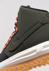 High-top sneaker in dark green with orange hardware, textured upper, white midsole, and patterned rubber outsole. Nike branding visible.