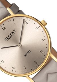 Montre à quartz avec un boîtier doré, un cadran argenté brossé, un bracelet en cuir gris, des marqueurs d'heure noirs et une couronne texturée.