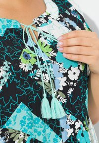 Kukkapuku, jossa on musta tausta, jossa on sinisiä, vihreitä ja valkoisia kuvioita. Sisältää sidottavan kaula-aukon ja vaaleansiniset tupsut.