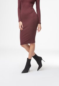 Burgundowa sukienka z długim rękawem, prążkowana, o dopasowanym kroju, w połączeniu z czarnymi dzianinowymi botkami za kostkę z wydłużonym noskiem i szpilką.
