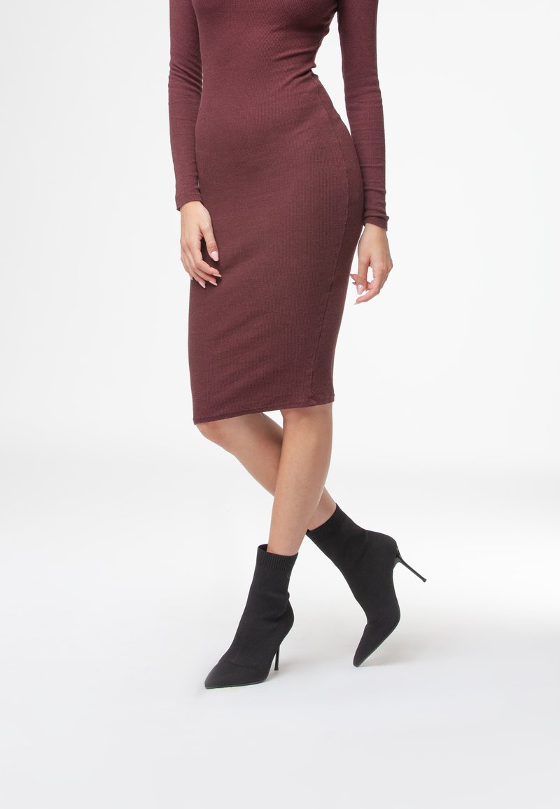 Burgundowa sukienka z długim rękawem, prążkowana, o dopasowanym kroju, w połączeniu z czarnymi dzianinowymi botkami za kostkę z wydłużonym noskiem i szpilką.
