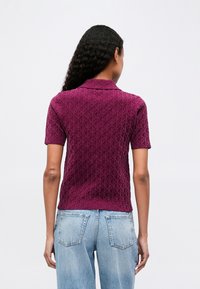 Lühikeste varrukatega tekstuuriga polo särk rikkas burgundi värvitoonis, millel on teemantmuster; omab sobivat lõiget ja klassikalist kraed. Kombineeritud heledate teksadega.